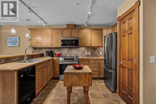 Kitchen and living area with light wood cabinets, stainless steel appliances, and a tiled backsplash. - 314, 170 Crossbow Place, Canmore