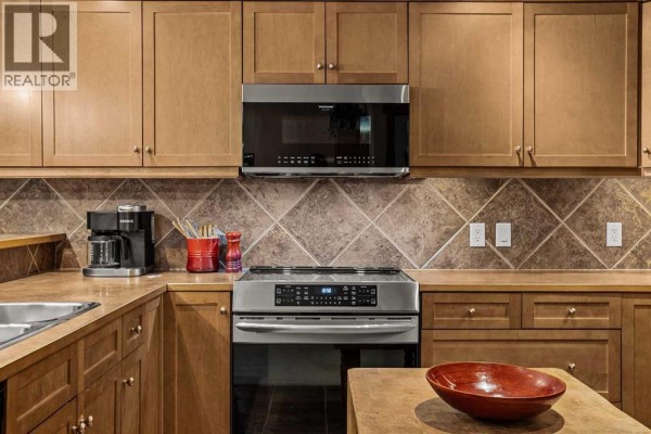 Close-up of the kitchen featuring wooden cabinets, stainless steel stove, and microwave above it. - 314, 170 Crossbow Place, Canmore
