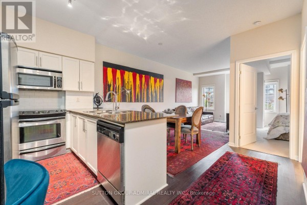 Kitchen with white cabinets, stainless steel appliances, granite countertop, and dining area with dark wood table. - 314 - 15 Windermere Avenue, Toronto