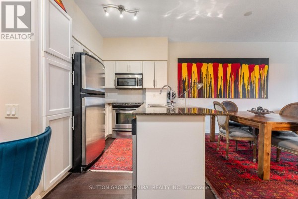 Kitchen with white cabinets, stainless steel appliances, granite countertop, and dining area with dark wood table. - 314 - 15 Windermere Avenue, Toronto