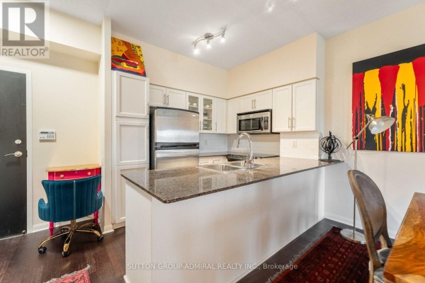 Kitchen with white cabinets, stainless steel appliances, granite countertop, and dining area with dark wood table and chairs. - 314 - 15 Windermere Avenue, Toronto