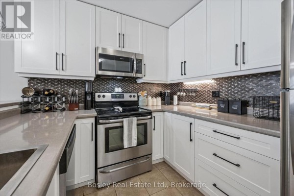 U-shaped kitchen with white cabinetry, stainless steel appliances, and a grey tiled backsplash. - 314 - 2 Colonial Drive, Guelph