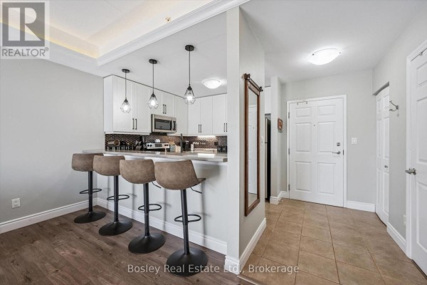 Open concept kitchen with white cabinets and a breakfast bar with four bar stools, adjacent to a tiled entryway. - 314 - 2 Colonial Drive, Guelph