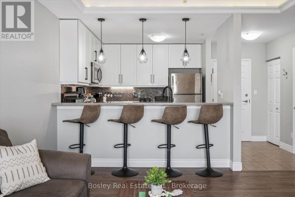 Kitchen island with bar stools and a view of the living room with a sectional sofa. - 314 - 2 Colonial Drive, Guelph