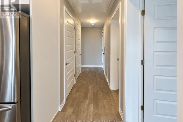 Hallway with wood-look flooring, multiple white doors, and a stainless steel appliance. - 314 - 470 Gordon Krantz Avenue, Milton