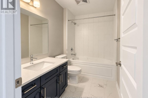 Bathroom with a dark blue vanity, white countertop, toilet, and white tiled bathtub. - 314 - 470 Gordon Krantz Avenue, Milton