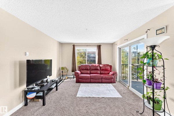 Living room with a red leather couch, TV, sliding glass doors to a balcony, and carpet. - #314 11820 22 Av Sw, Edmonton