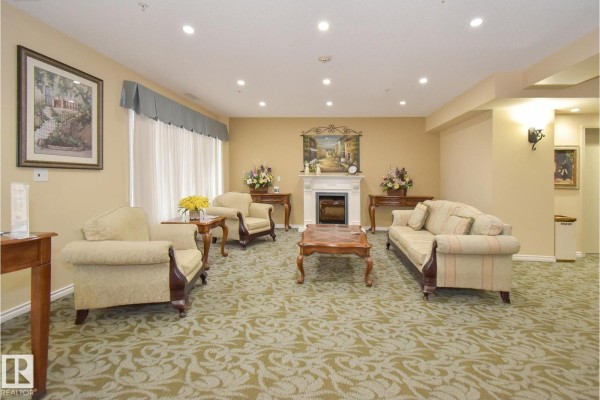 Lounge area with a fireplace, upholstered seating, coffee table, and decorative art. - #314 9820 165 St Nw, Edmonton