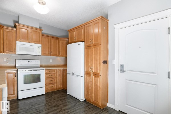 Compact kitchen with light wood cabinets, white appliances, and dark laminate flooring. - #314 9820 165 St Nw, Edmonton