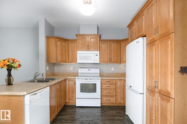 Kitchen features light wood cabinetry, white appliances, and a stainless steel sink. - #314 9820 165 St Nw, Edmonton