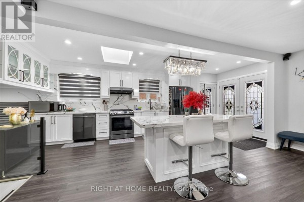 Open-concept kitchen and dining area featuring a white island, sleek cabinetry, and a crystal chandelier. - 314 Morrish Road S, Toronto