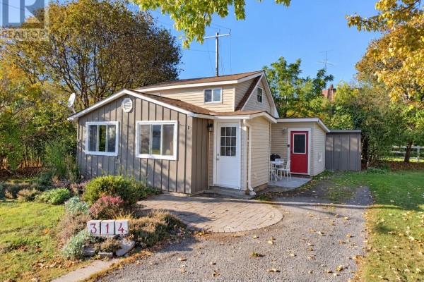Side exterior of a grey cottage with red door and outdoor seating area. - 314 Second Avenue, Prince Edward County