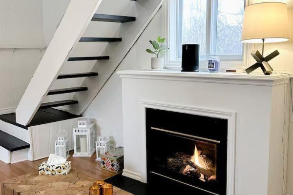 Living room fireplace with black surround and white mantelpiece, next to stairs. - 314 Second Avenue, Prince Edward County