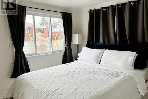 Bedroom with a white duvet, black headboard, and large window with dark curtains. - 314 Second Avenue, Prince Edward County