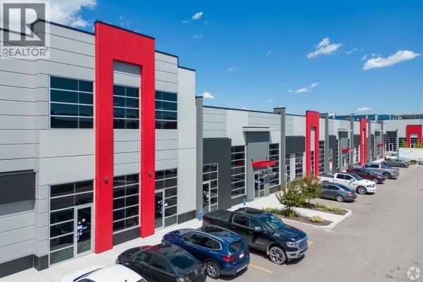 Exterior view of commercial units with grey and red paneling, large windows, and parking lot. - 3140, 6520 36 Street Ne, Calgary