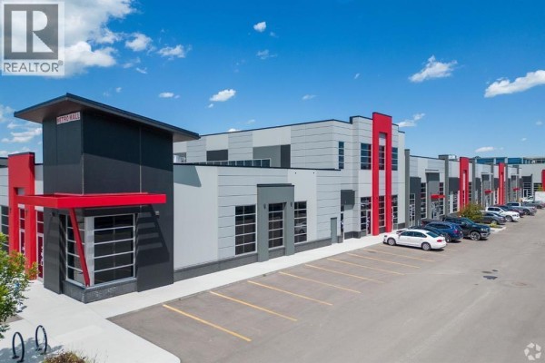 Close-up exterior view of a commercial building with grey, black, and red facade and parking. - 3140, 6520 36 Street Ne, Calgary