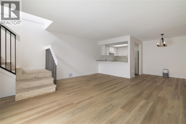 Living area and kitchen pass-through with light wood-look flooring and carpeted stairs. - 3140 Wilson Street Unit# 916, Penticton