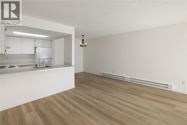 Kitchen and living space with white cabinets, stainless steel fridge, and wood-look flooring. - 3140 Wilson Street Unit# 916, Penticton