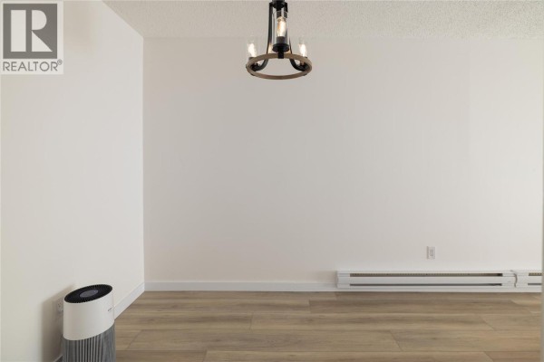 Empty living room space with wood-look flooring and a modern chandelier light fixture. - 3140 Wilson Street Unit# 916, Penticton