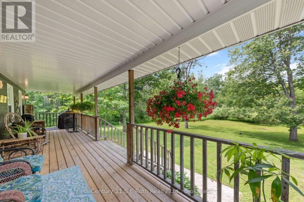View from the covered front porch of a dark grey house, showing wooden deck, railings, and a green backyard. - 3147 Dalton Court, Tay