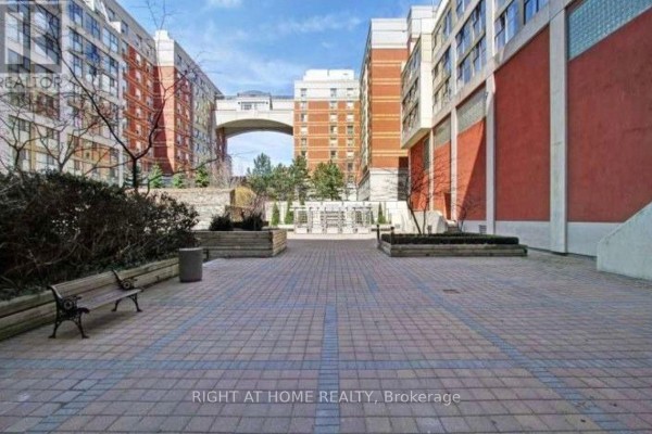 Courtyard area with stone pavers, a wooden bench, and planters surrounded by brick buildings. - 315 - 222 The Esplanade, Toronto