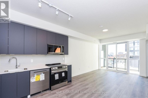 Apartment kitchen with dark grey cabinets, stainless steel stove, and a view of the living area and balcony. - 315 - 225 Malta Avenue, Brampton