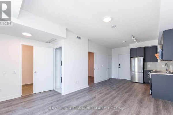 Open concept living area with a kitchen, dark grey cabinets, and doorways to other rooms. - 315 - 225 Malta Avenue, Brampton