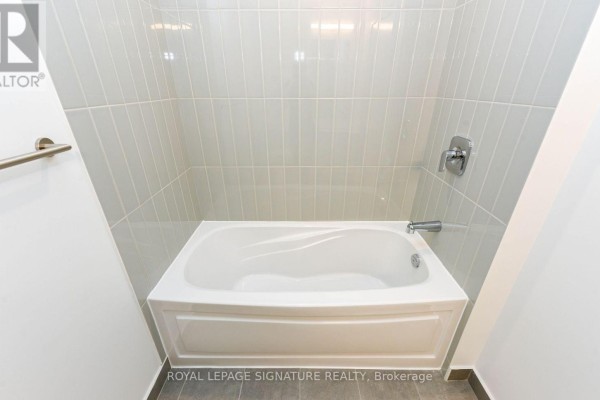 White bathtub with light grey tiled walls in a modern bathroom. - 315 - 225 Malta Avenue, Brampton