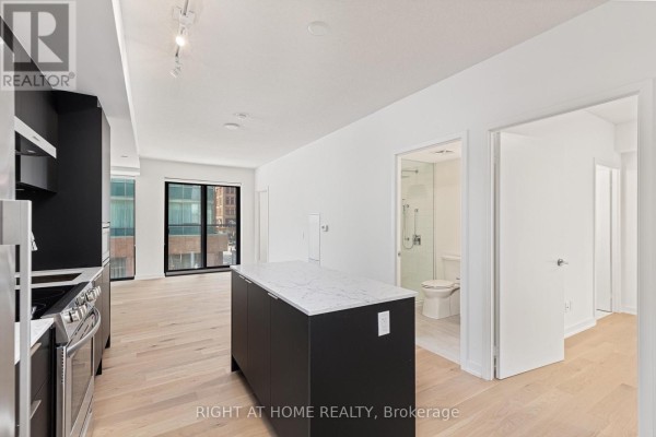 Open concept living area with a black kitchen island with a white countertop, overlooking a hallway. - 315 - 25 Richmond Street E, Toronto