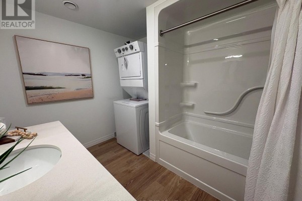 A small bathroom with a white bathtub, shower curtain, stacked washer and dryer, and vanity. - 509 - 351 Hill Street, London East