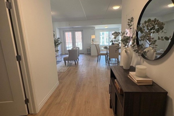 Hallway view into an open-concept living and dining area with light wood floors and a large mirror. - 509 - 351 Hill Street, London East