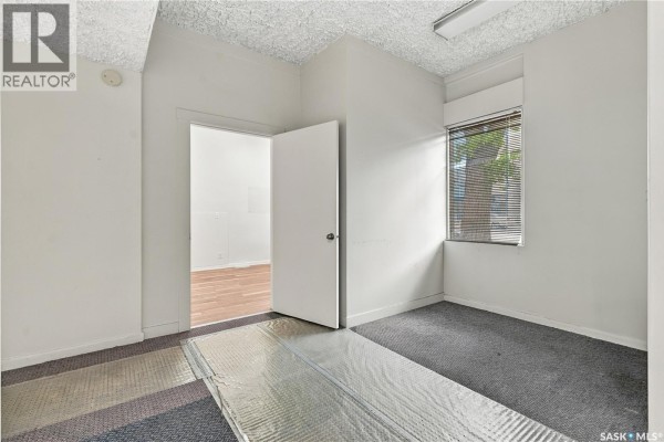 Empty office room with grey carpet, white walls, and a window with blinds. - 315 20th Street E, Saskatoon