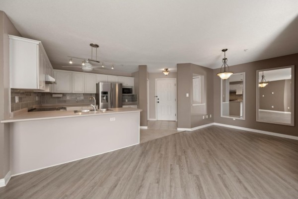Living room and kitchen area with light wood floors, white cabinets, beige walls, and large mirrors. - 315 22150 48 Avenue, Langley