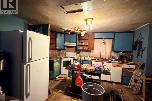 Kitchen with white refrigerator, stove, sink, and disheveled counters and flooring. - 315 3rd Avenue W, Assiniboia