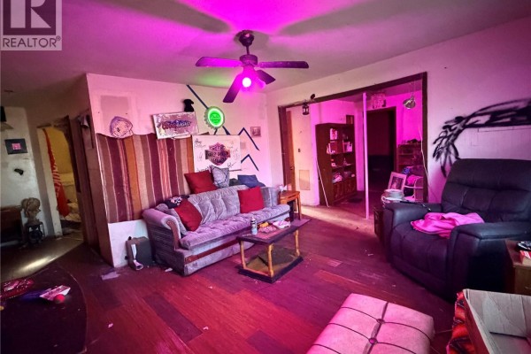 Living room with pink lighting, a grey sofa, black recliner, and hardwood floors. - 315 3rd Avenue W, Assiniboia