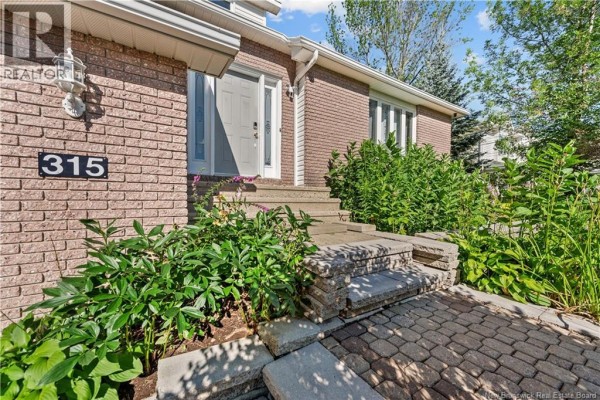 Front entrance with brick facade, light gray door, stone steps, and paved walkway. - 315 Belliveau, Dieppe