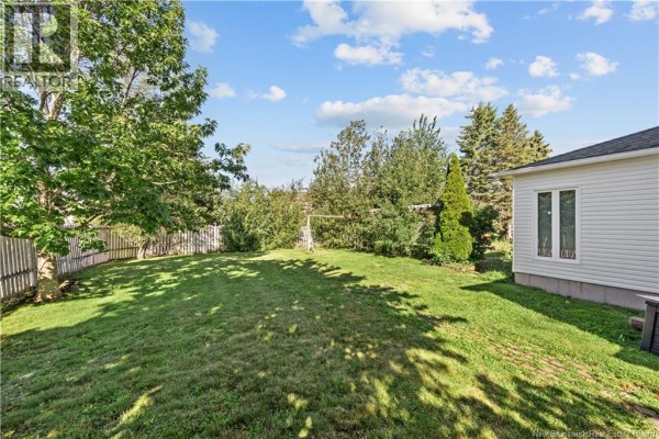 Backyard with green grass, mature trees, a fence, and a white vinyl-sided house section. - 315 Belliveau, Dieppe
