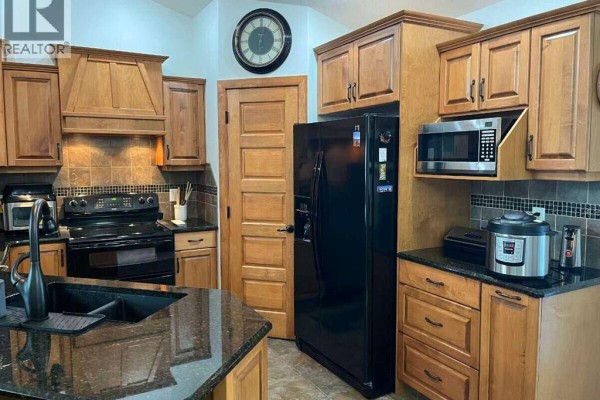 Kitchen with light oak cabinets, black appliances, granite countertops, and a dark granite sink. - 315 Centennial Avenue, Nobleford