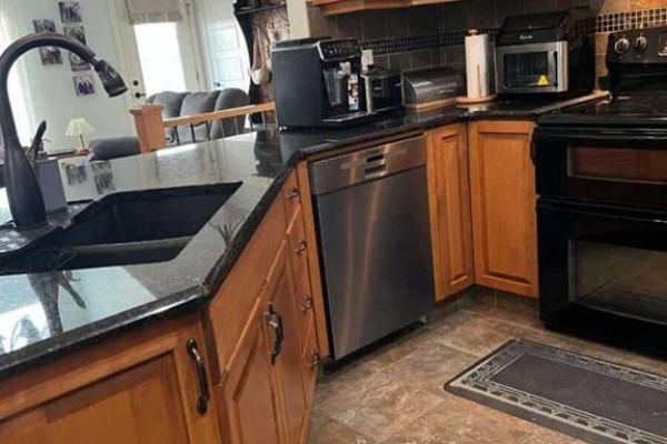 Kitchen island with a dark granite countertop, sink, dishwasher, and light oak cabinets. - 315 Centennial Avenue, Nobleford