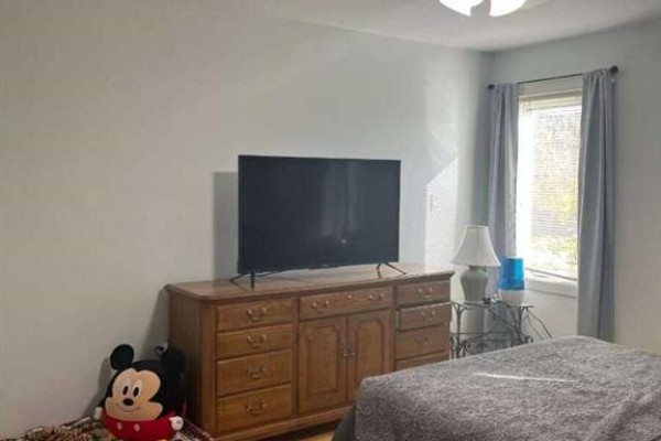 Bedroom with a large television on a wooden dresser, a bed, and a window with grey curtains. - 315 Centennial Avenue, Nobleford