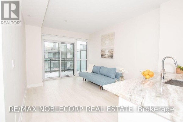 Living area with light wood floors, a blue sofa, and sliding glass doors. - 316 - 301 Sea Ray Avenue, Innisfil