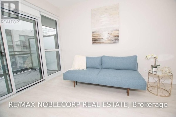 Living area with a blue sofa, side table, and sliding glass balcony doors. - 316 - 301 Sea Ray Avenue, Innisfil