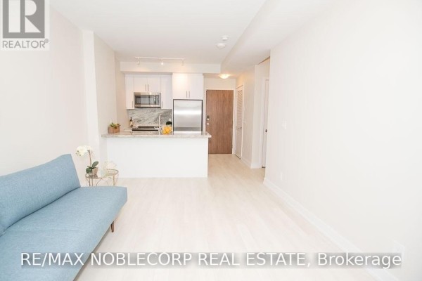 Open concept living and kitchen area with white walls and light wood floors. - 316 - 301 Sea Ray Avenue, Innisfil