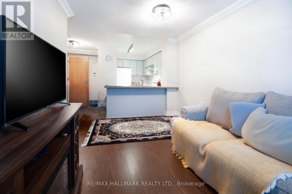 Living area with a sofa, television, and a view into the adjacent kitchen. - 316 - 62 Suncrest Boulevard, Markham