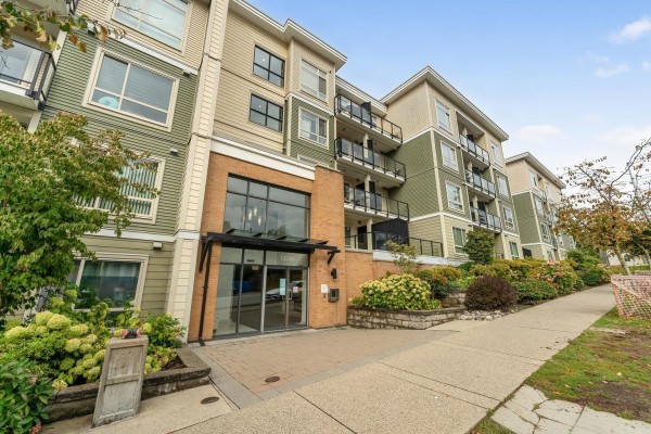 Exterior front view of a multi-story apartment building with brick and green siding. - 316 13789 107a Avenue, Surrey