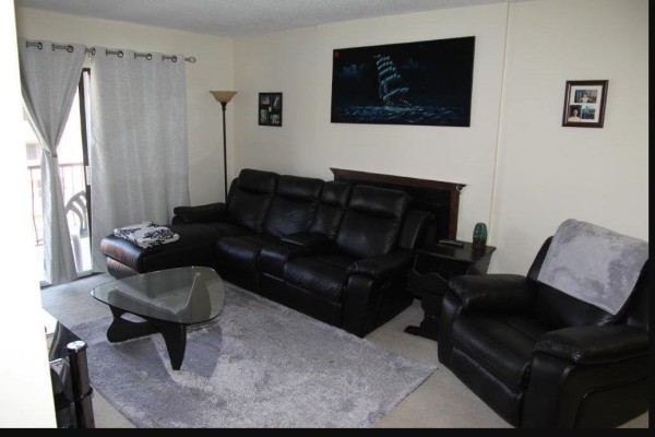 Living room with black leather sectional, glass coffee table, gray rug, and balcony access. - 316 45749 Spadina Street, Chilliwack Downtown, Chilliwack