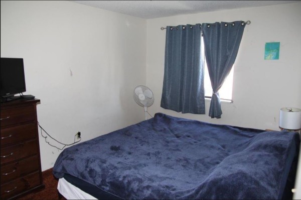 Bedroom with a large blue bed, dark wood dresser, television, and blue curtains. - 316 45749 Spadina Street, Chilliwack Downtown, Chilliwack