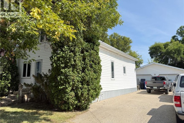 Side view of a white house with trees and a detached garage. - 316 4th Street, Weyburn