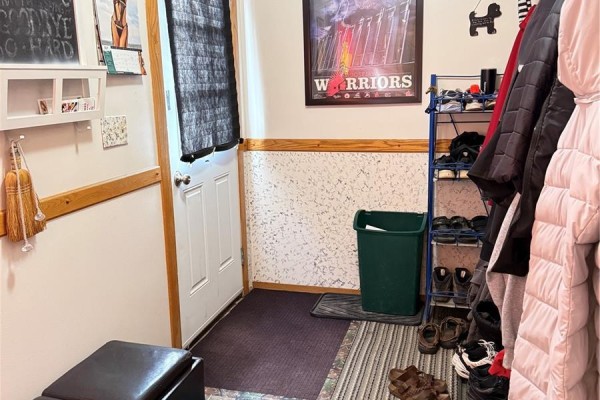 Mudroom with coat rack, shoe rack, trash can, and textured wallpaper. - 316 4th Street, Weyburn