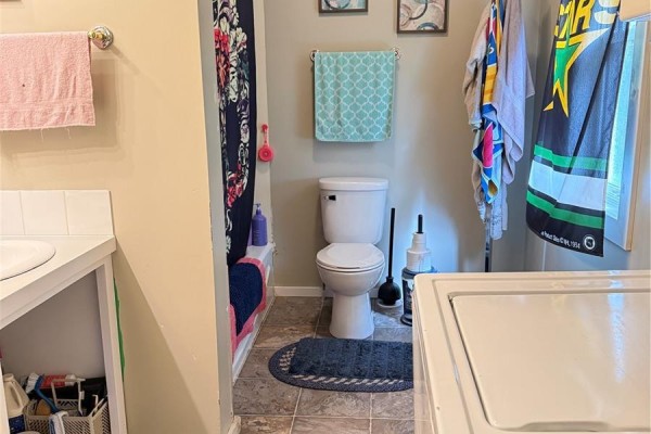 Small bathroom with toilet, bathtub, shower curtain, and tiled floor. - 316 4th Street, Weyburn